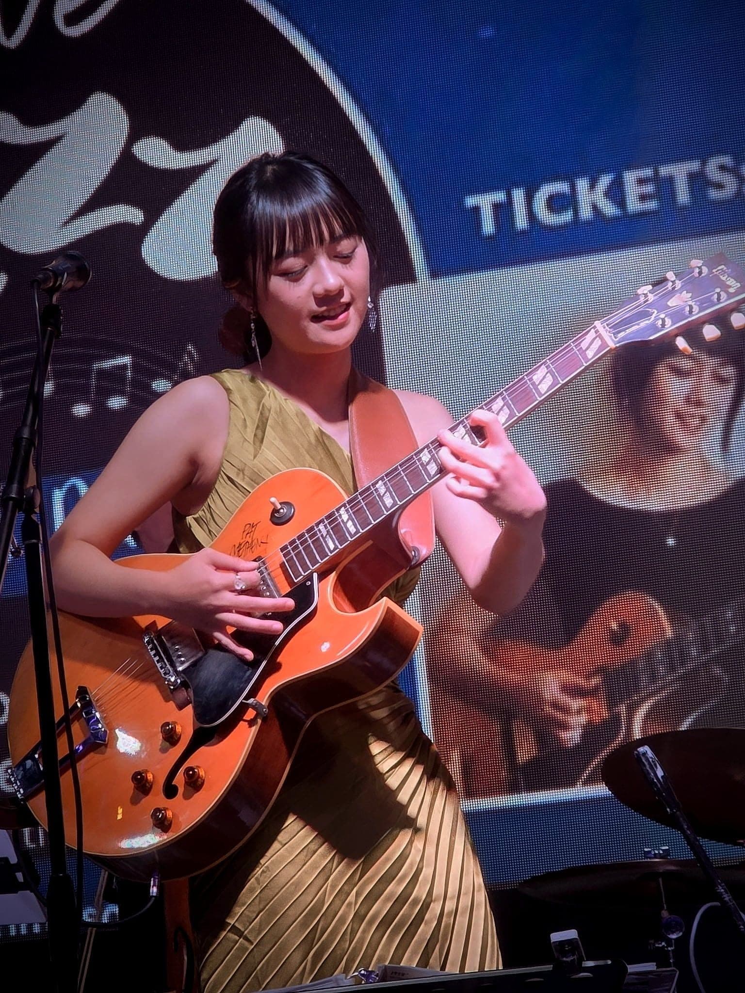 A guitarist and vocalist performing with her quintet under stage lights.