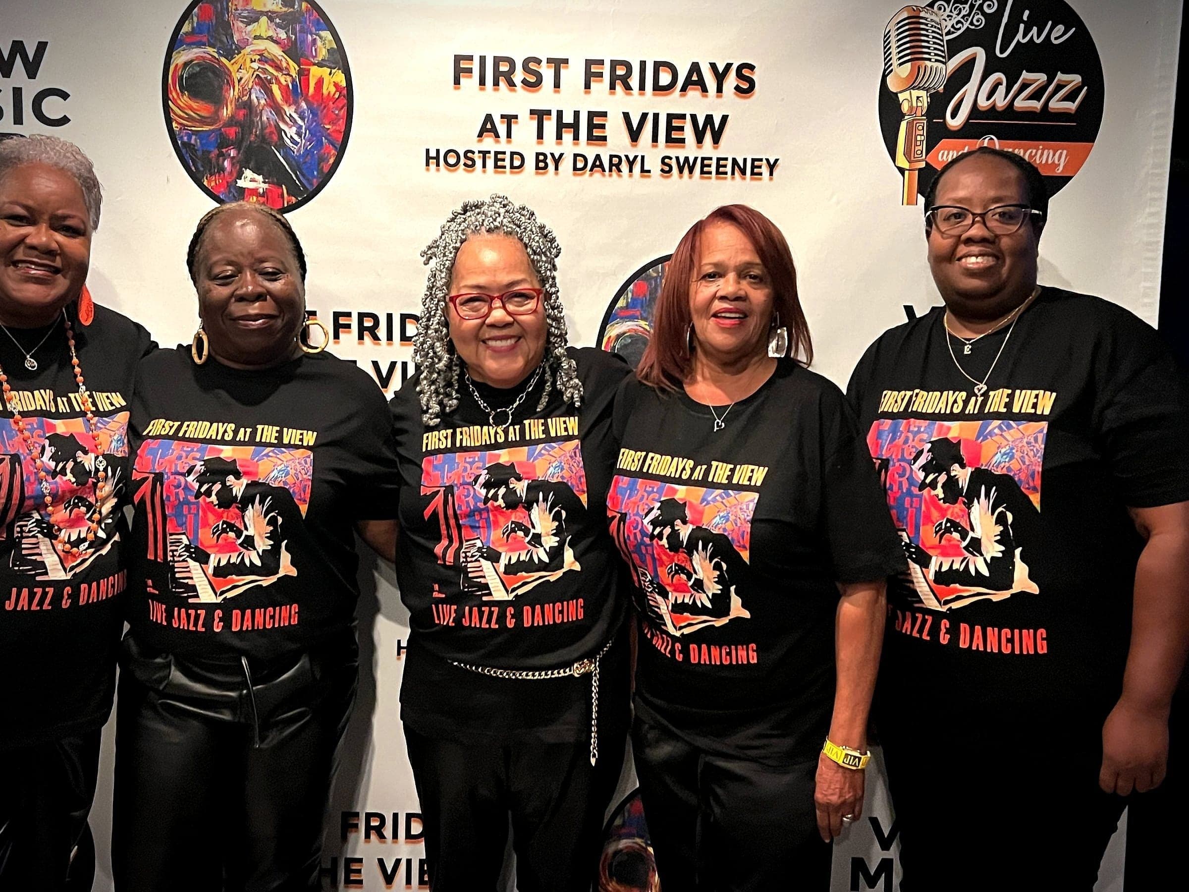 Five supporters in First Fridays event shirts at the venue step-and-repeat.