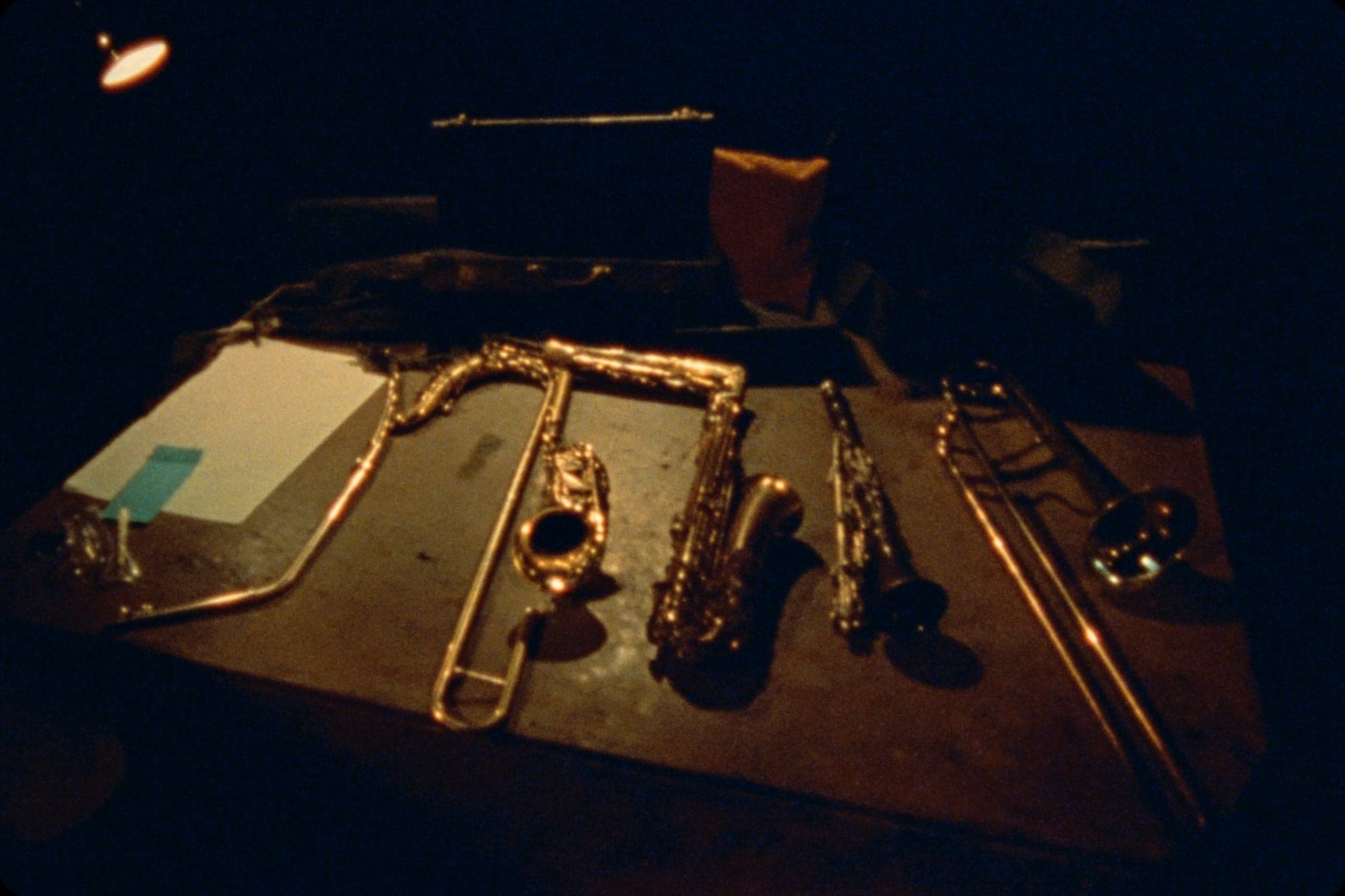 Restored brass and woodwind instruments laid out on a worn wooden table under warm light, cases open behind them.