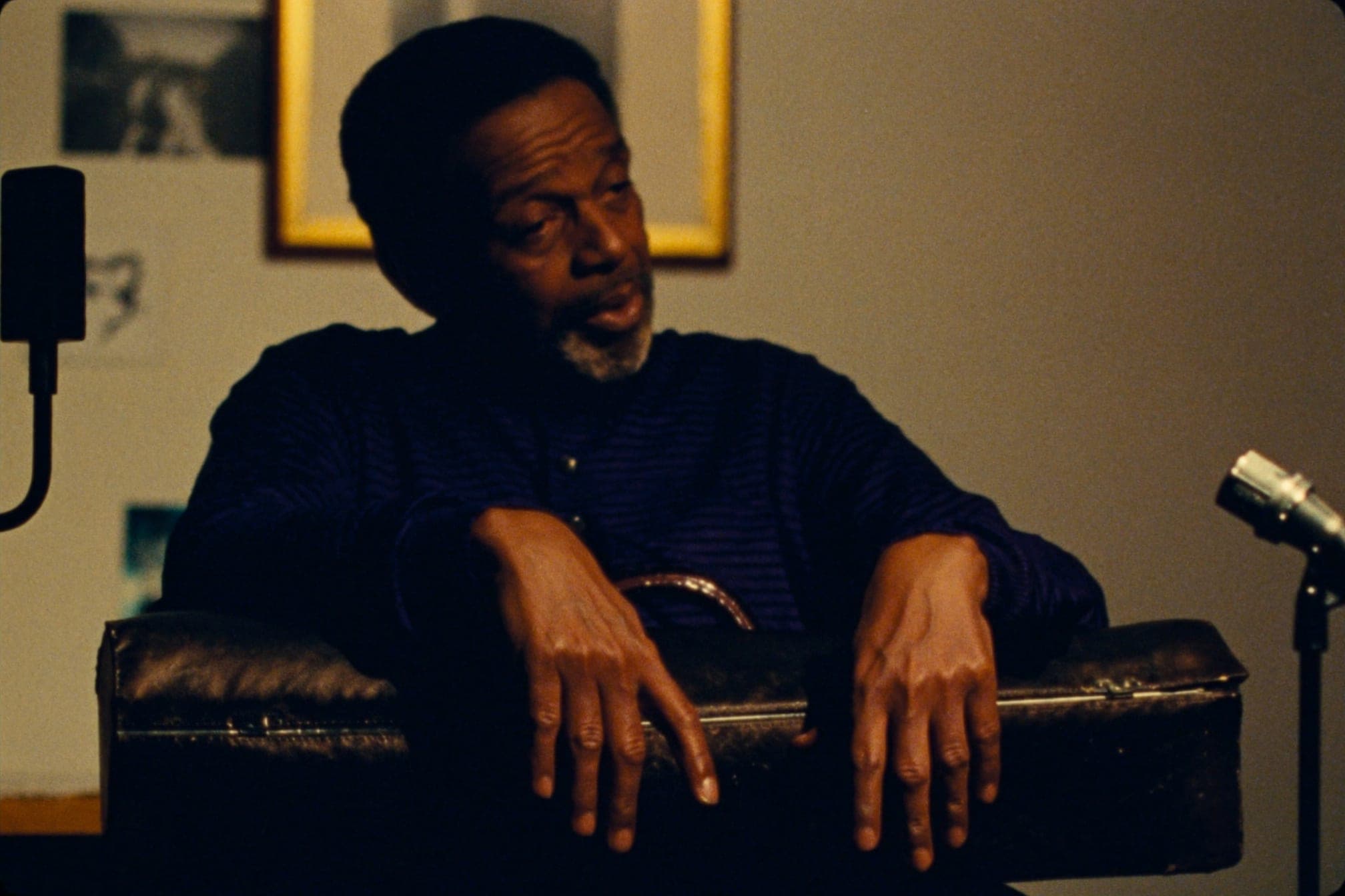 An elder musician seated for a recorded oral-history interview, hands resting on a trumpet case.