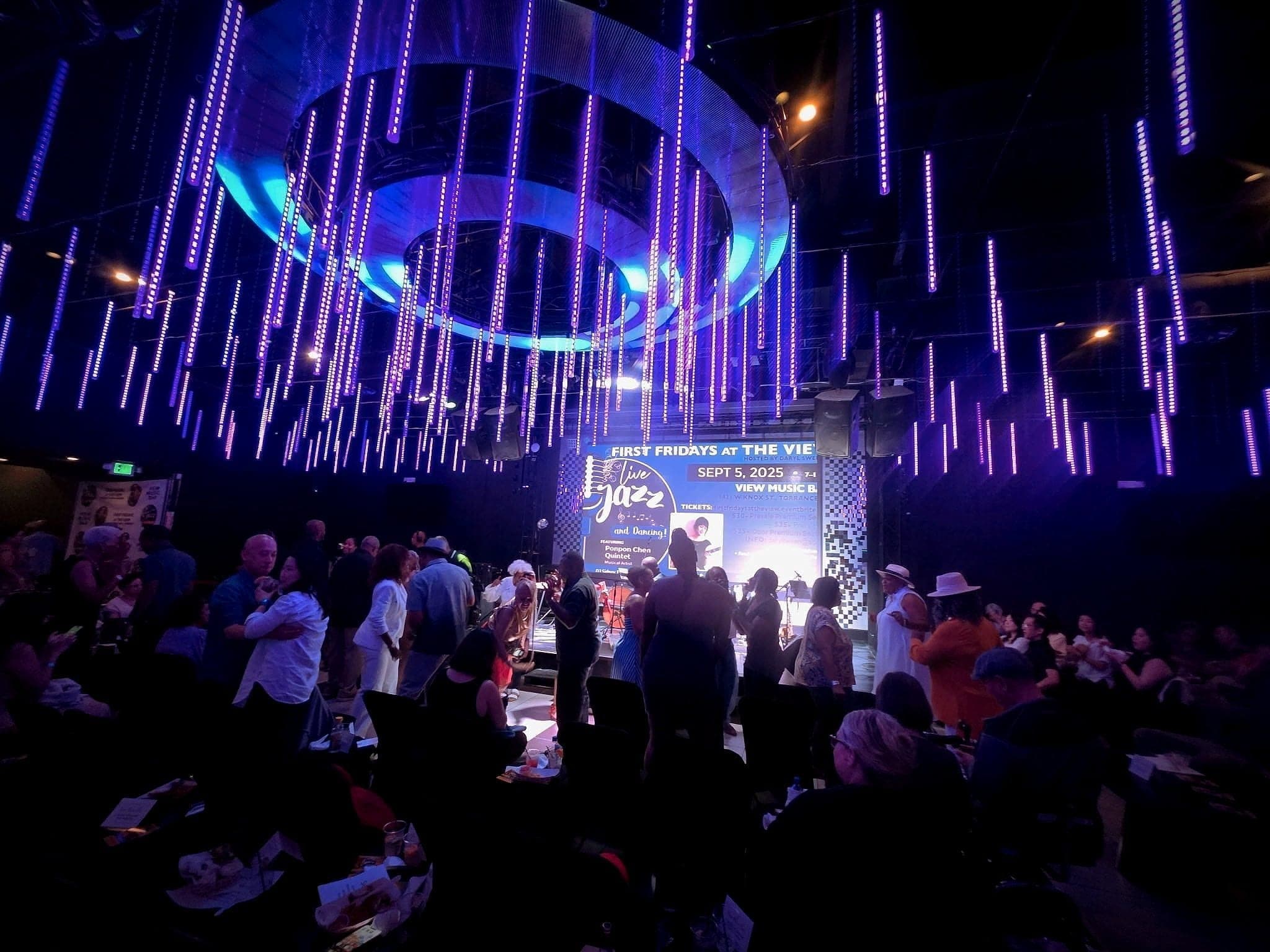A packed room at a First Fridays concert, couples dancing near the stage under the venue's lights.
